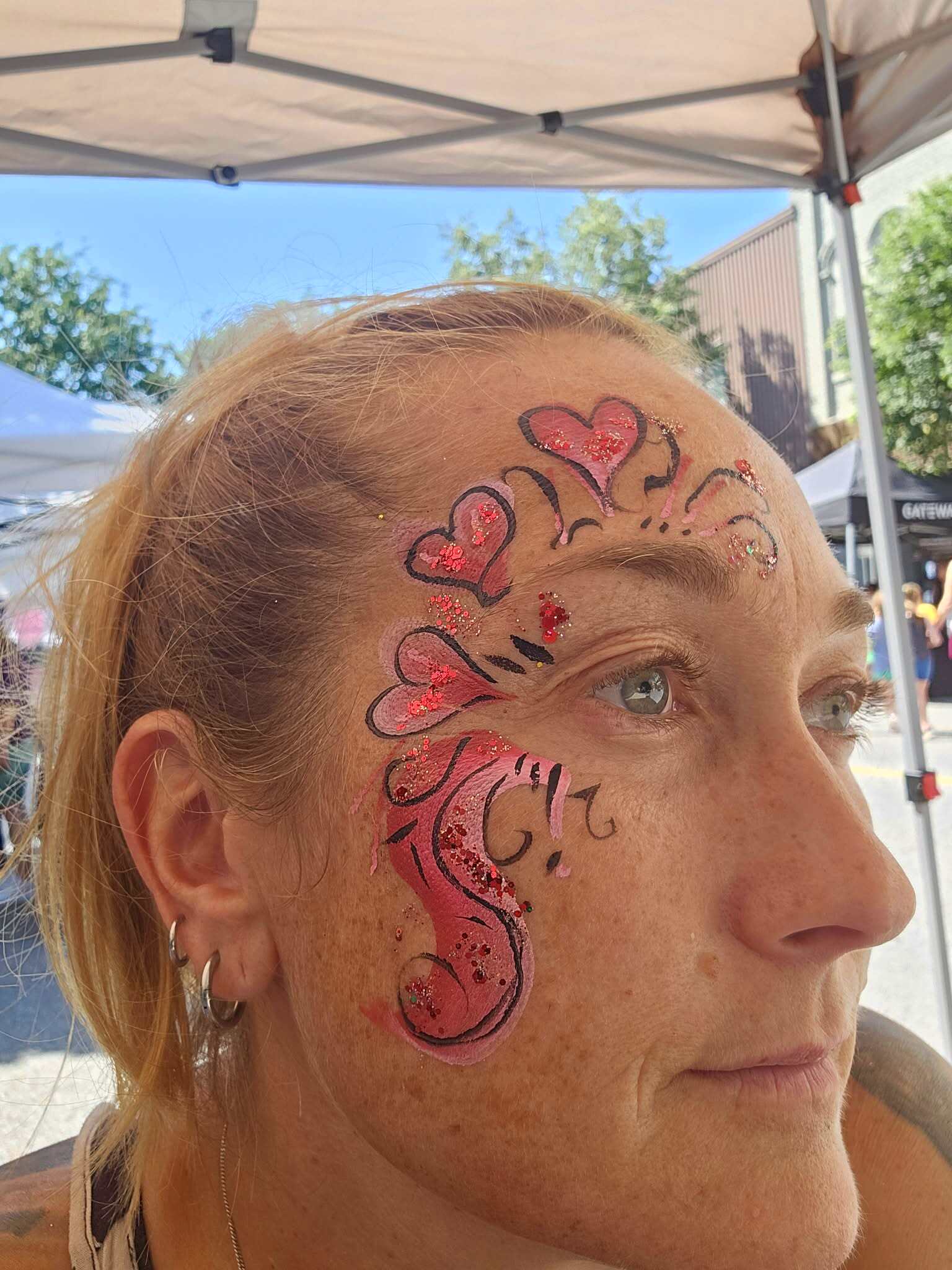 Woman with pink and red glittery hearts and swirls painted around her eye