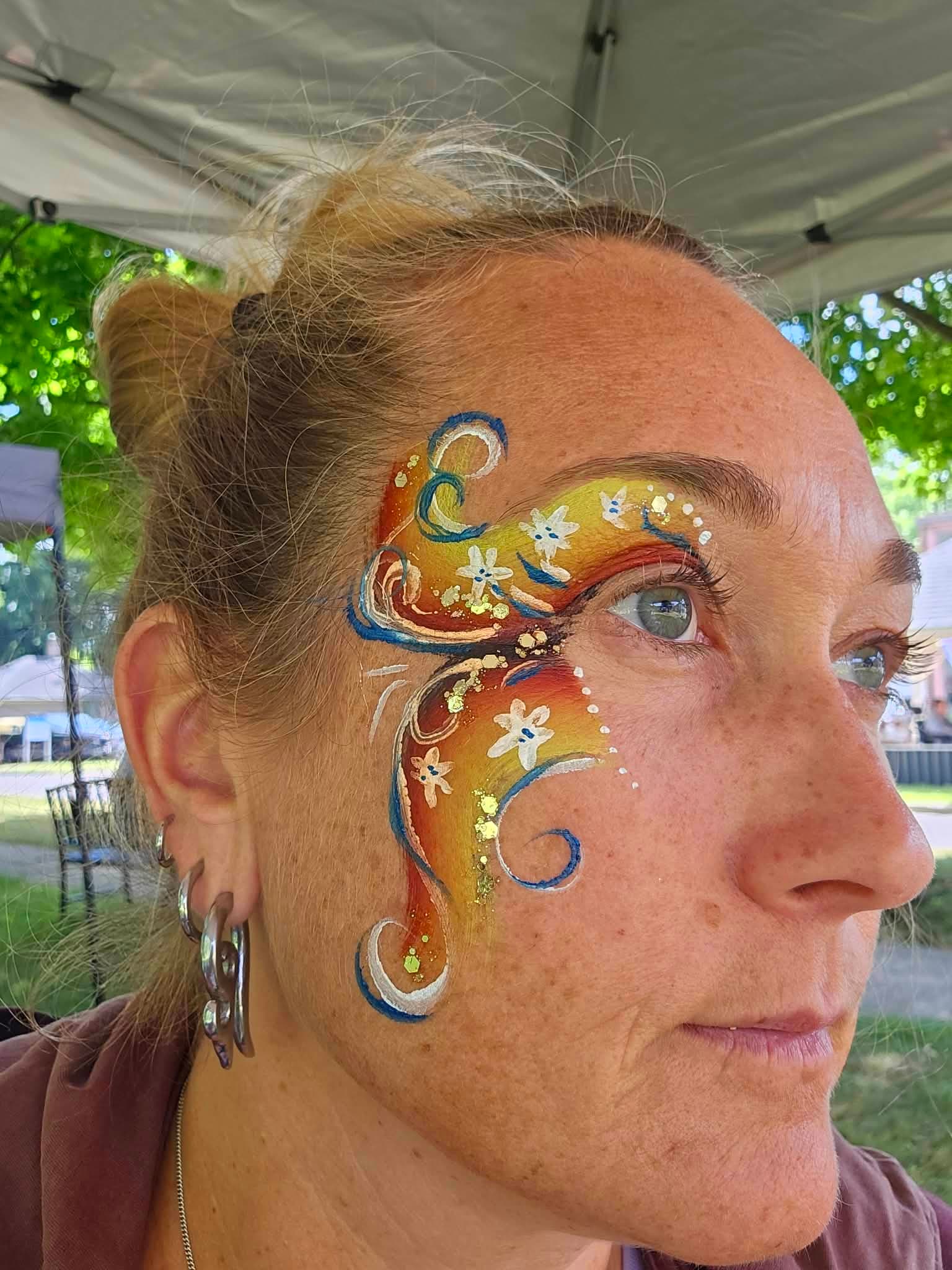 Woman with golden swirls and white flowers painted around her eye
