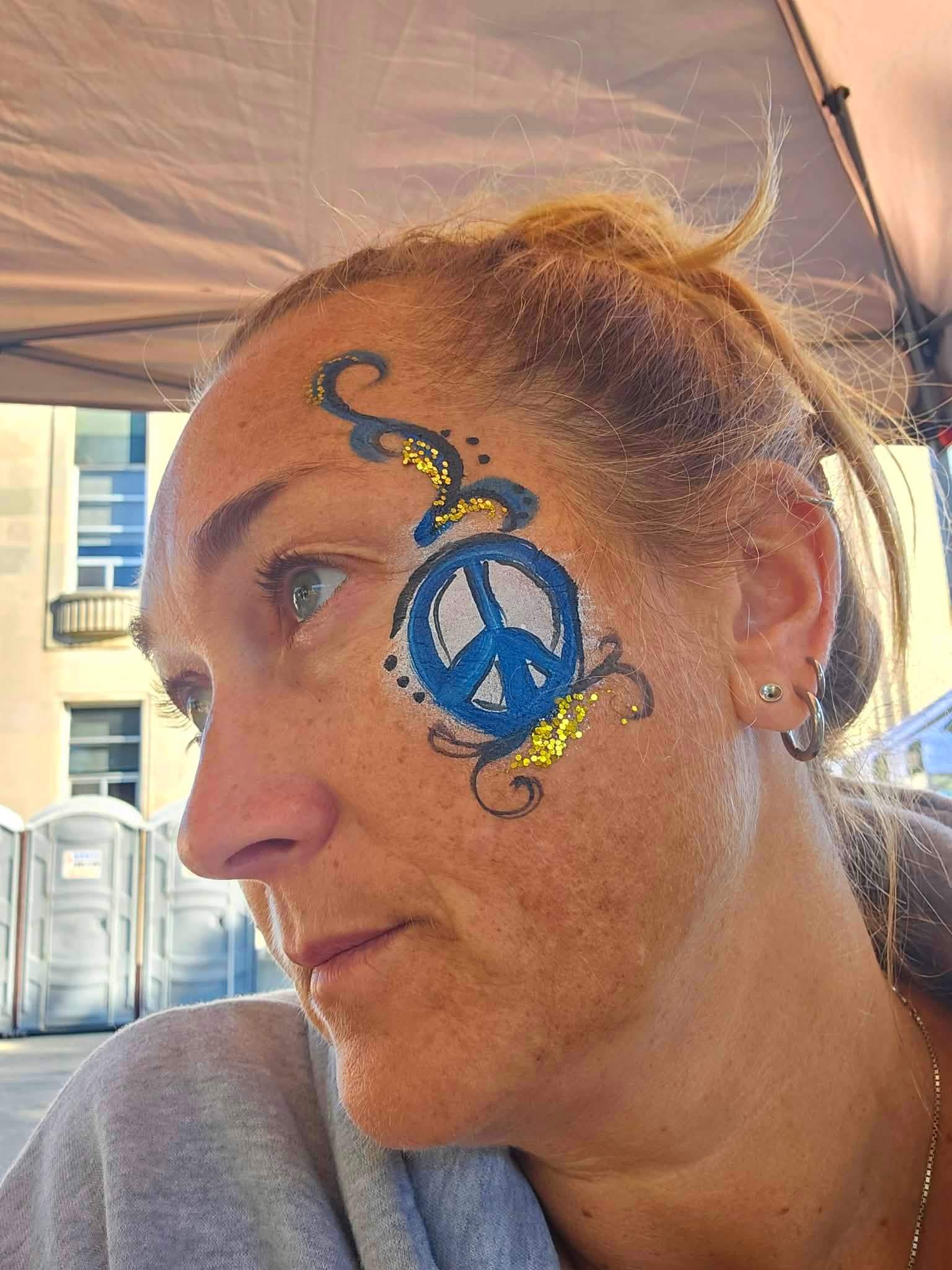 Woman with a blue peace sign and gold glitter painted on her cheek