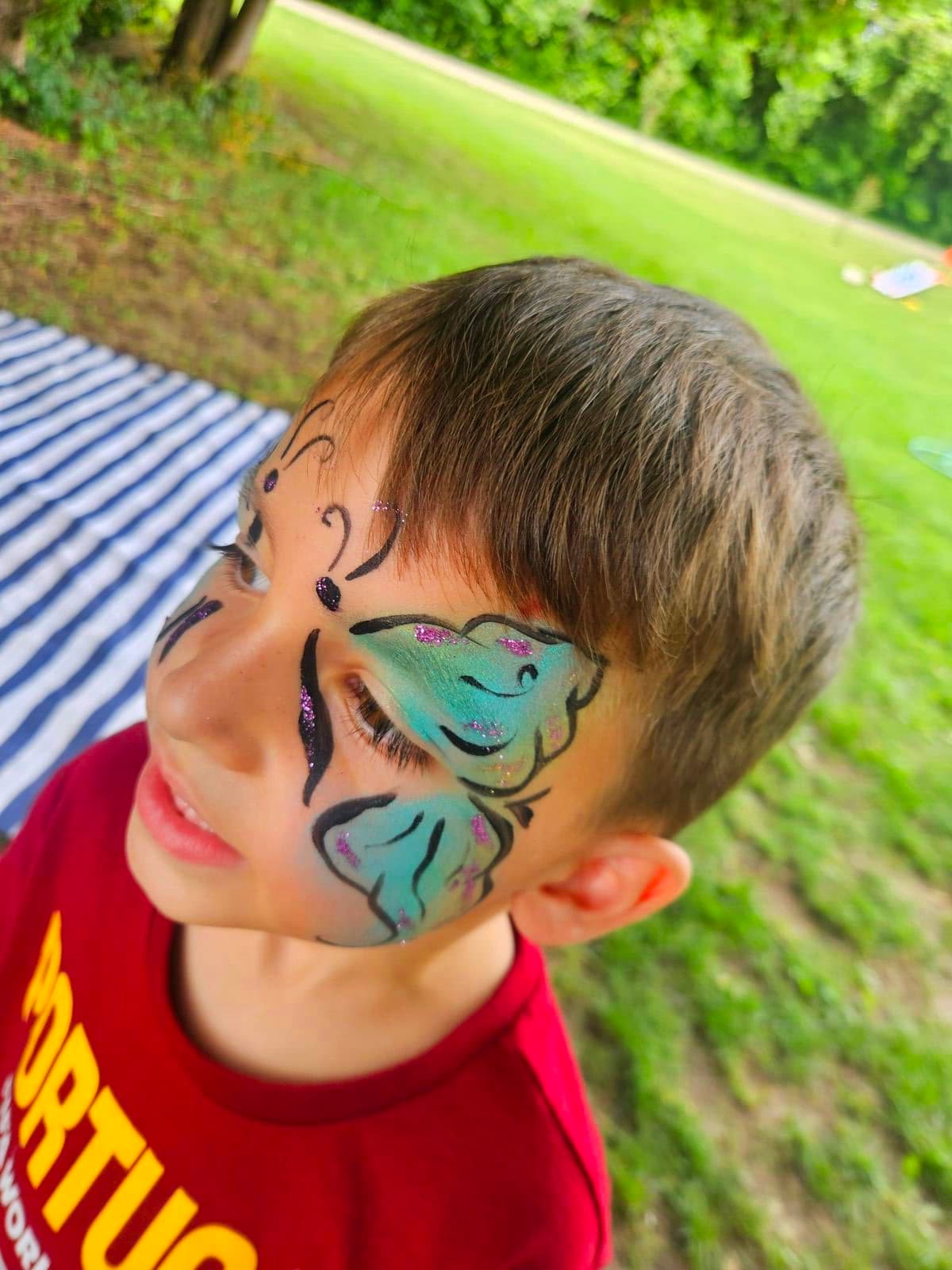 Boy with a teal glitter butterfly painted across his eyes