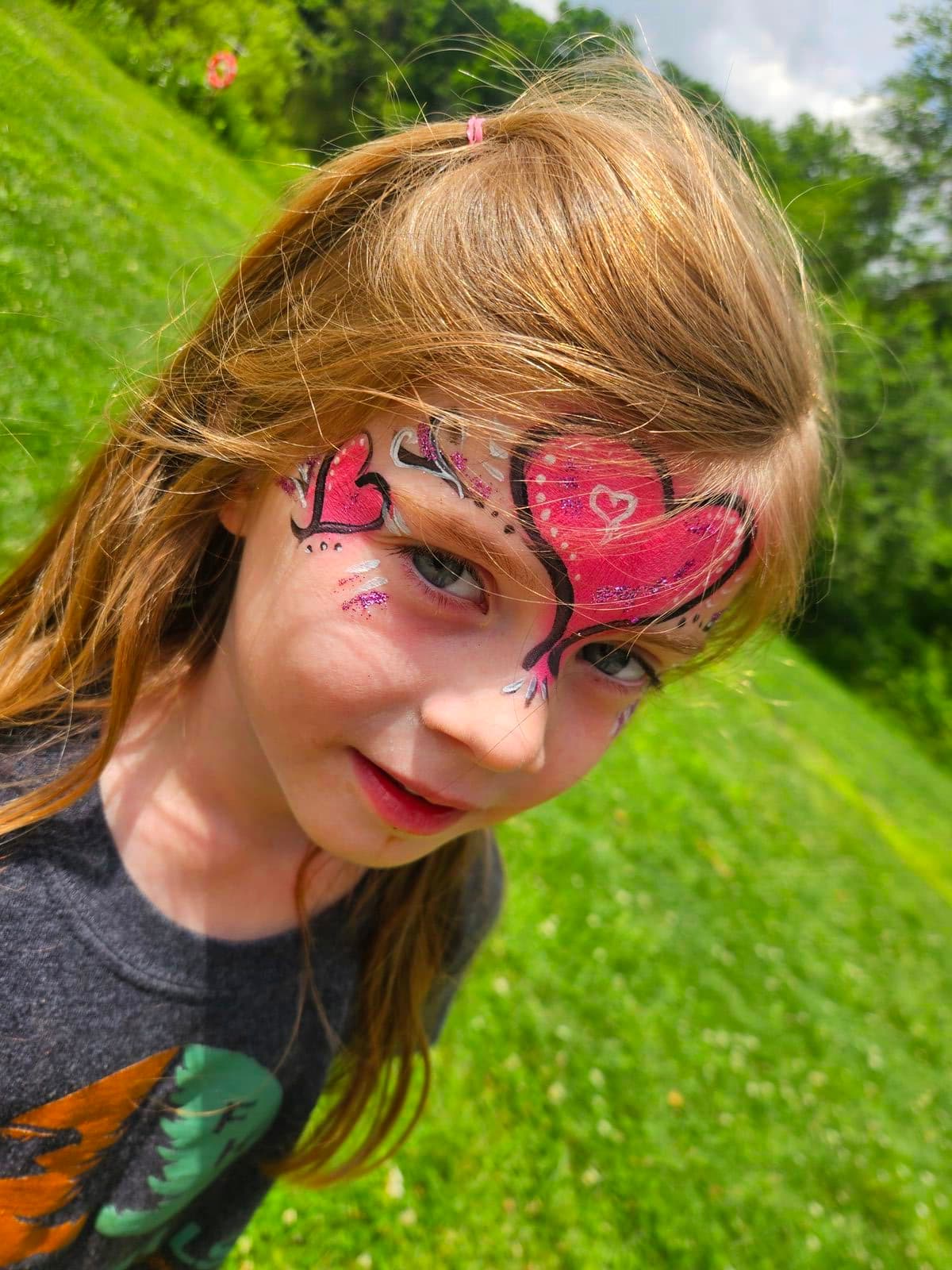 Girl with glittery pink hearts painted on her forehead and cheek
